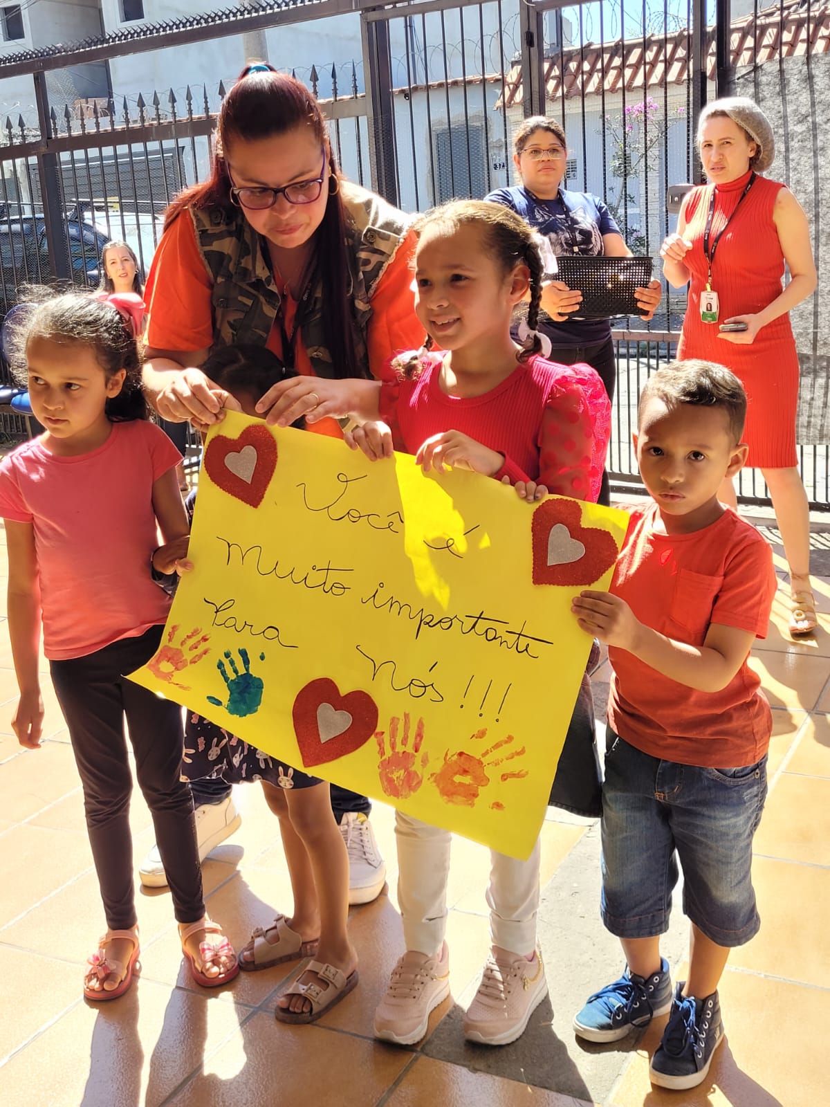 Na imagem, três crianças seguram um cartaz amarelo, com os dizeres: Você é muito importante para nós!, com desenhos de mão colorida e corações.